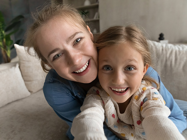 younger girl holding camera and smiling while older girl has arms around her and is also smiling