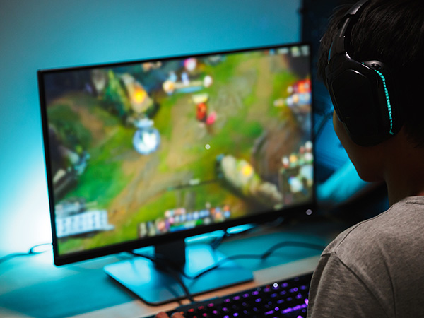 a gamer with headphones on looking at a large monitor showing some type of video game